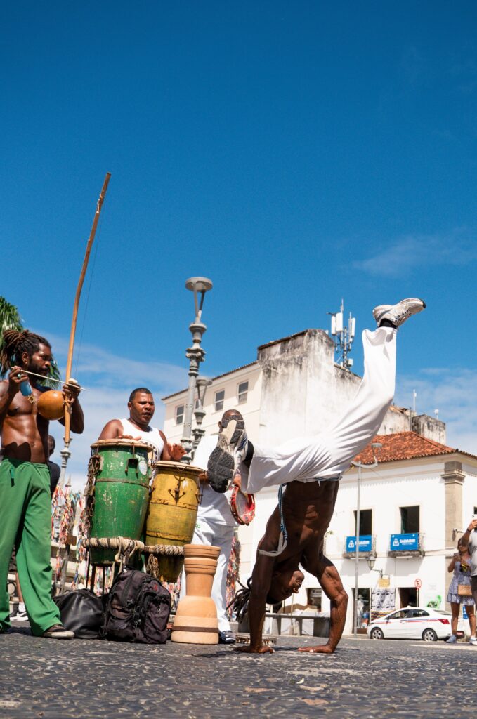 Mannen die capoeira beoefenen op een historisch, met kasseien bestraat plein in Brazilië onder een strakblauwe lucht.