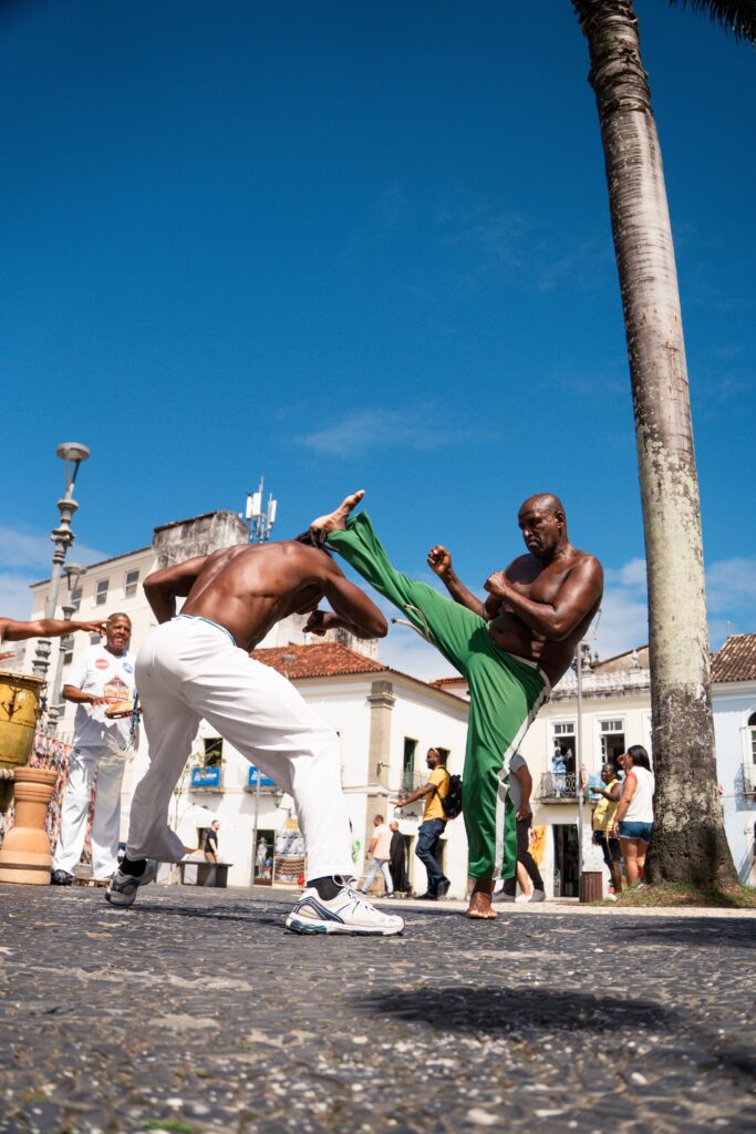 Mannen die capoeira beoefenen op een historisch, met kasseien bestraat plein in Brazilië onder een strakblauwe lucht.